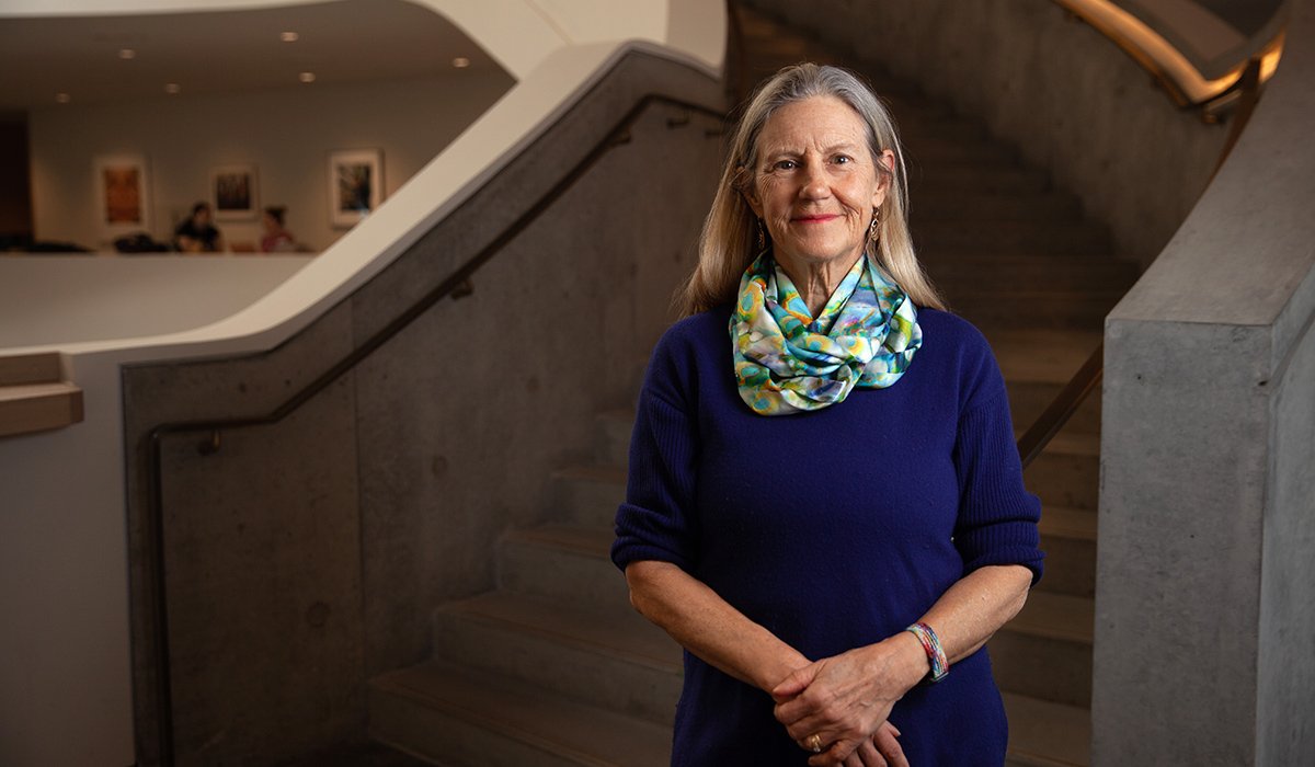 An image of Linda Duxbury wearing a blue sweater and a colourful scarf. She is standing next to a concrete staircase.